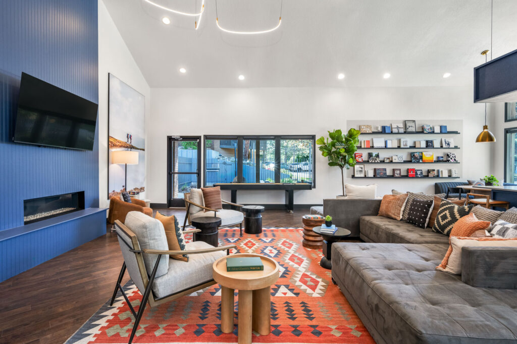 Large communal sitting space with chairs and sectional couch facing a wall mounted television above an electric fireplace.