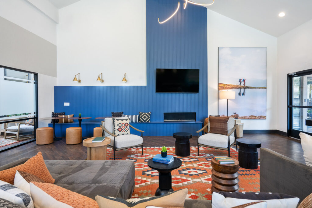 Large communal sitting space with chairs and sectional couch facing a wall mounted television above an electric fireplace.
